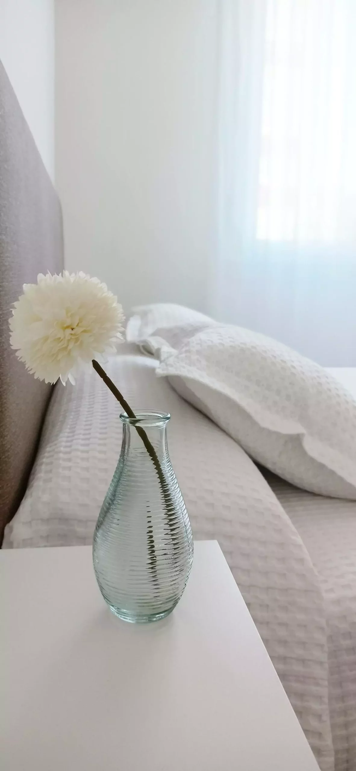 Detalle decorativo, un jarrón con una flor, en la mesilla de noche del dormitorio principal, con cama de matrimonio